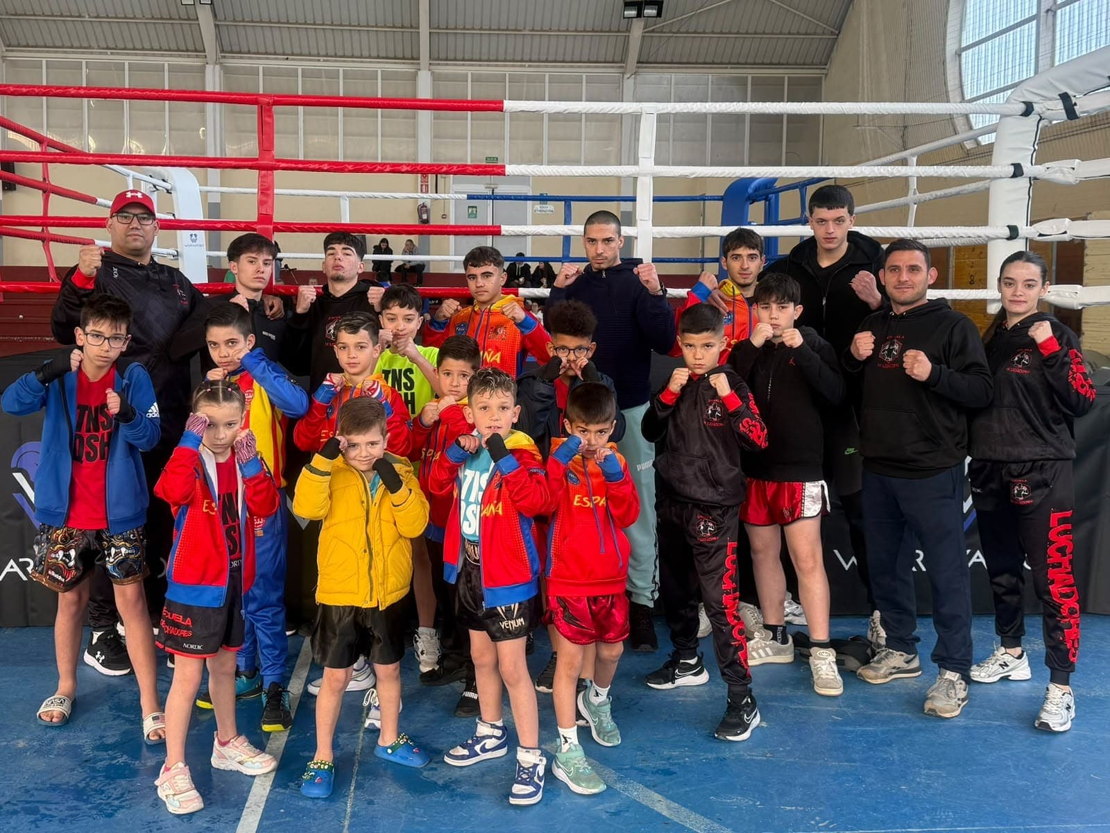 El grupo de niños de la escuela, con sus entrenadores, posa junto al ring en un campeonato de kickboxing
